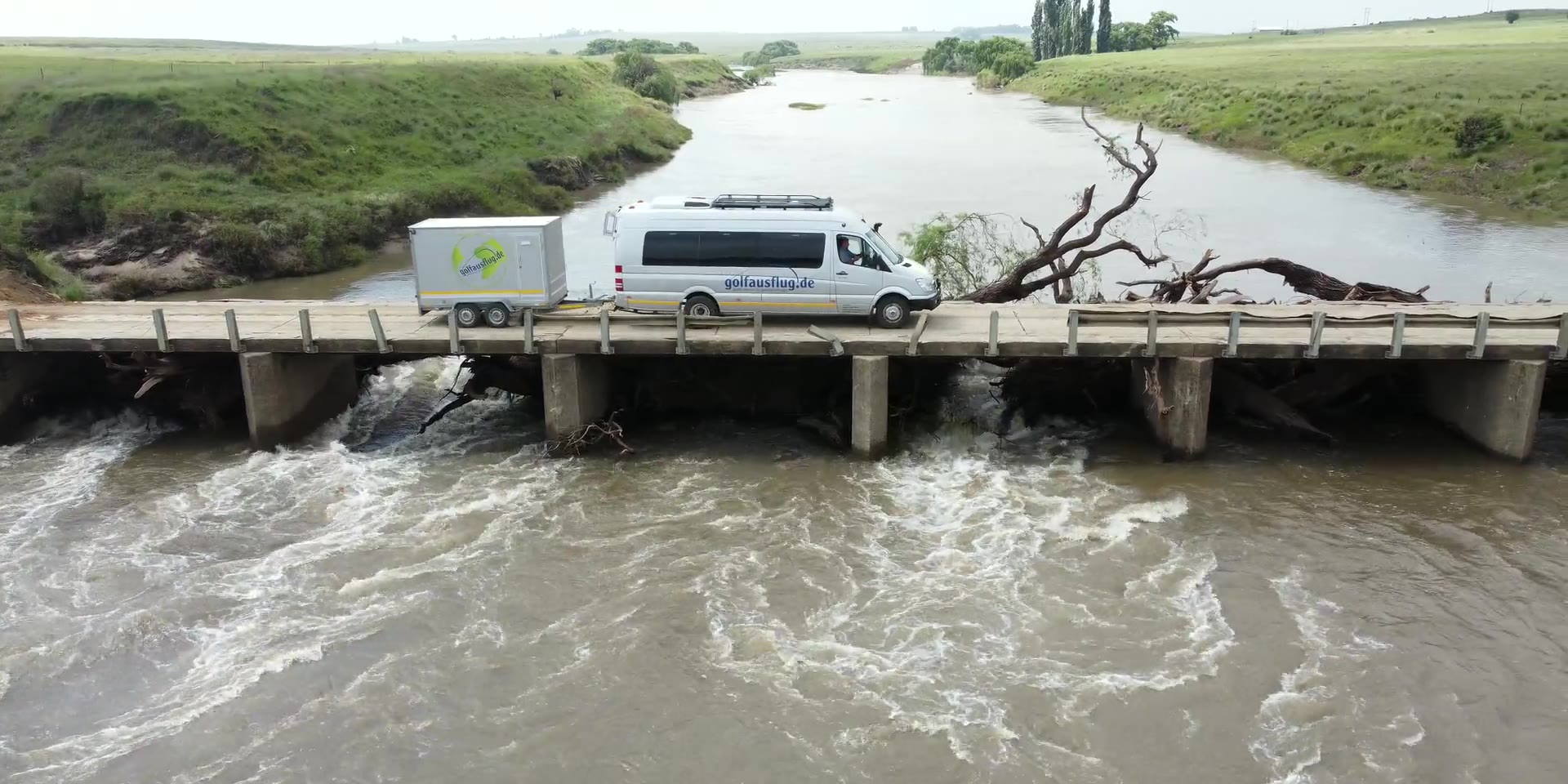 Der Reisebus von golfausflug.de mit Anhänger fährt über eine Flussbrücke in Südafrika, aus der Luft gefilmt